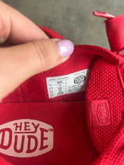Close-up of a red Hey Dude shoe interior showing the size label and a finger with light purple nail polish touching the inside lining
