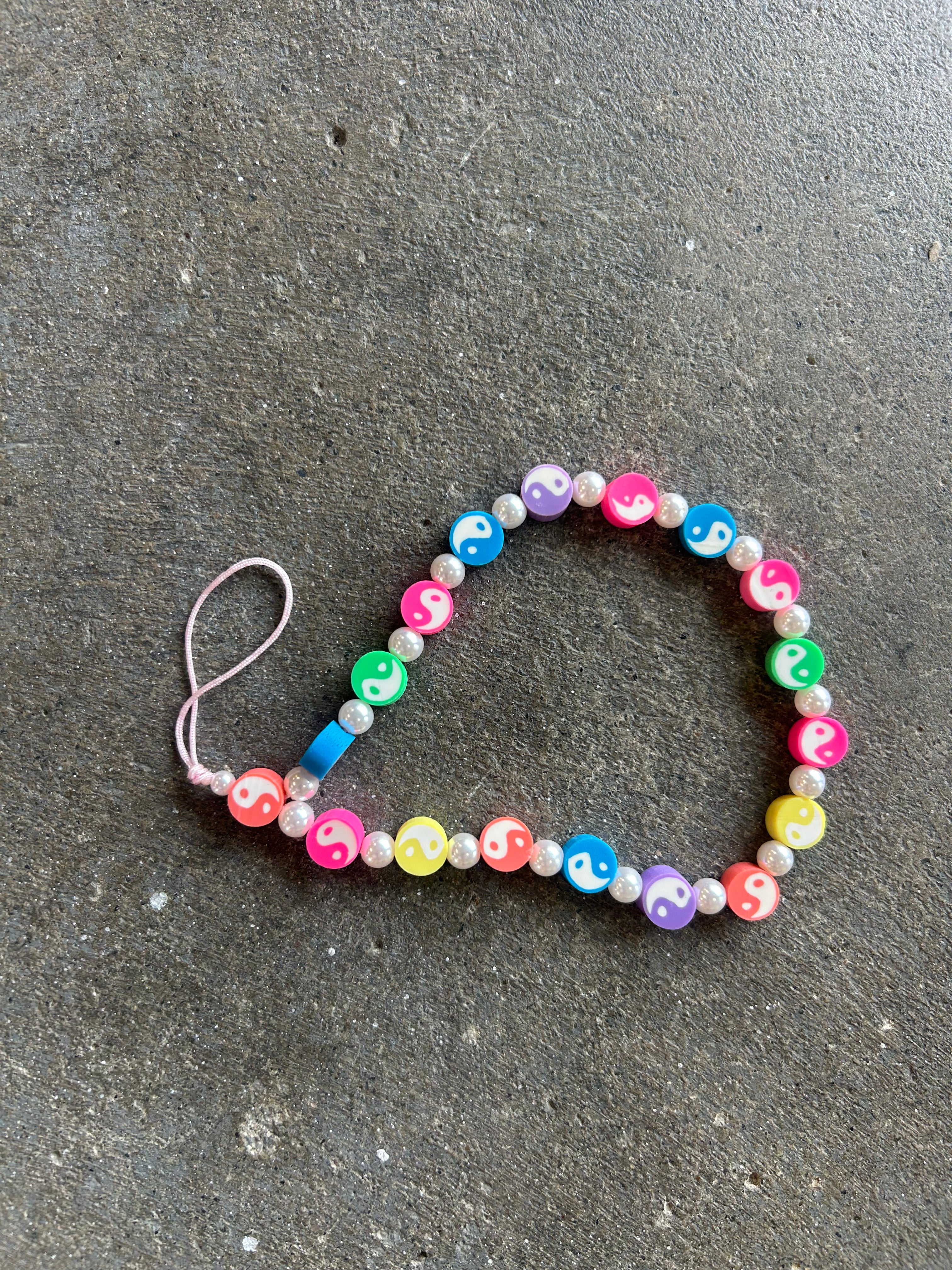 Multi Color Yin yang phone charm bracelet on a concrete surface