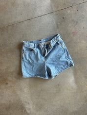 Light wash blue denim shorts laid flat on a concrete floor