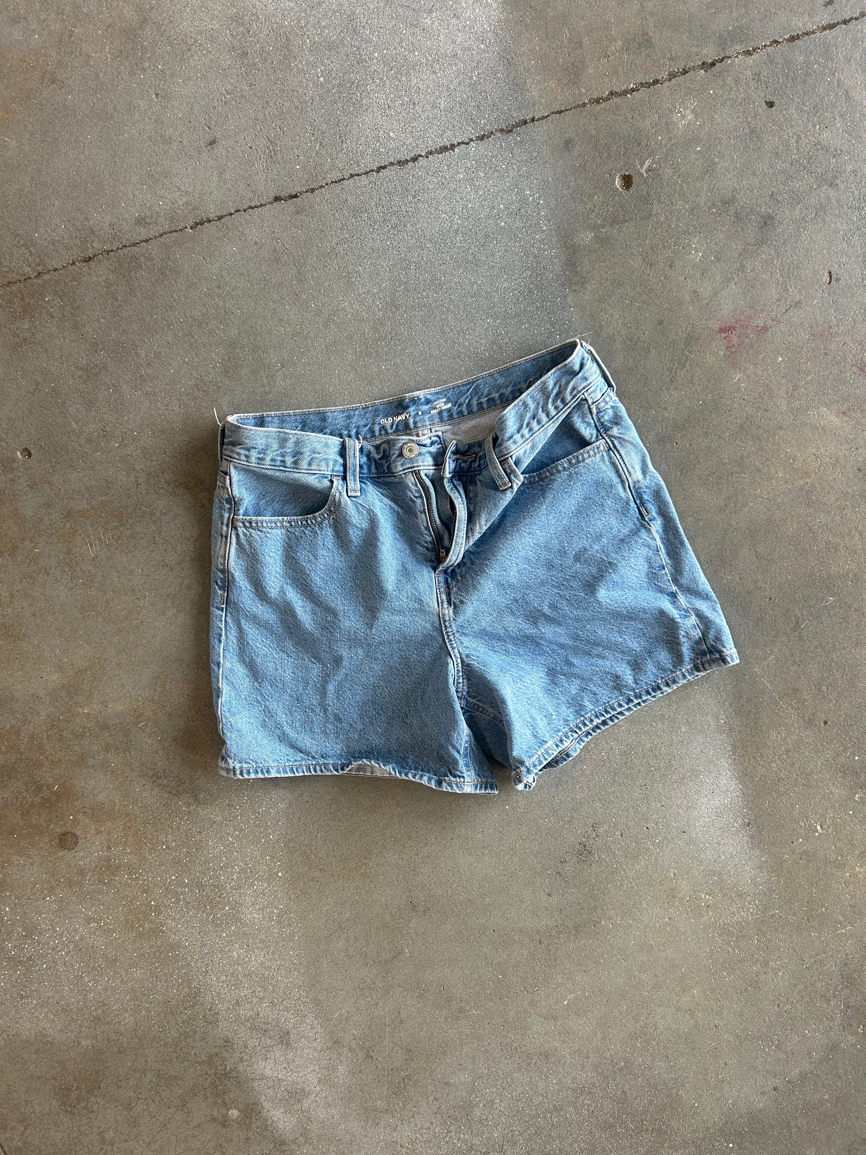 Light wash blue denim shorts laid flat on a concrete floor