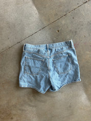 Light wash blue denim shorts shown from the back, laid flat on a concrete floor
