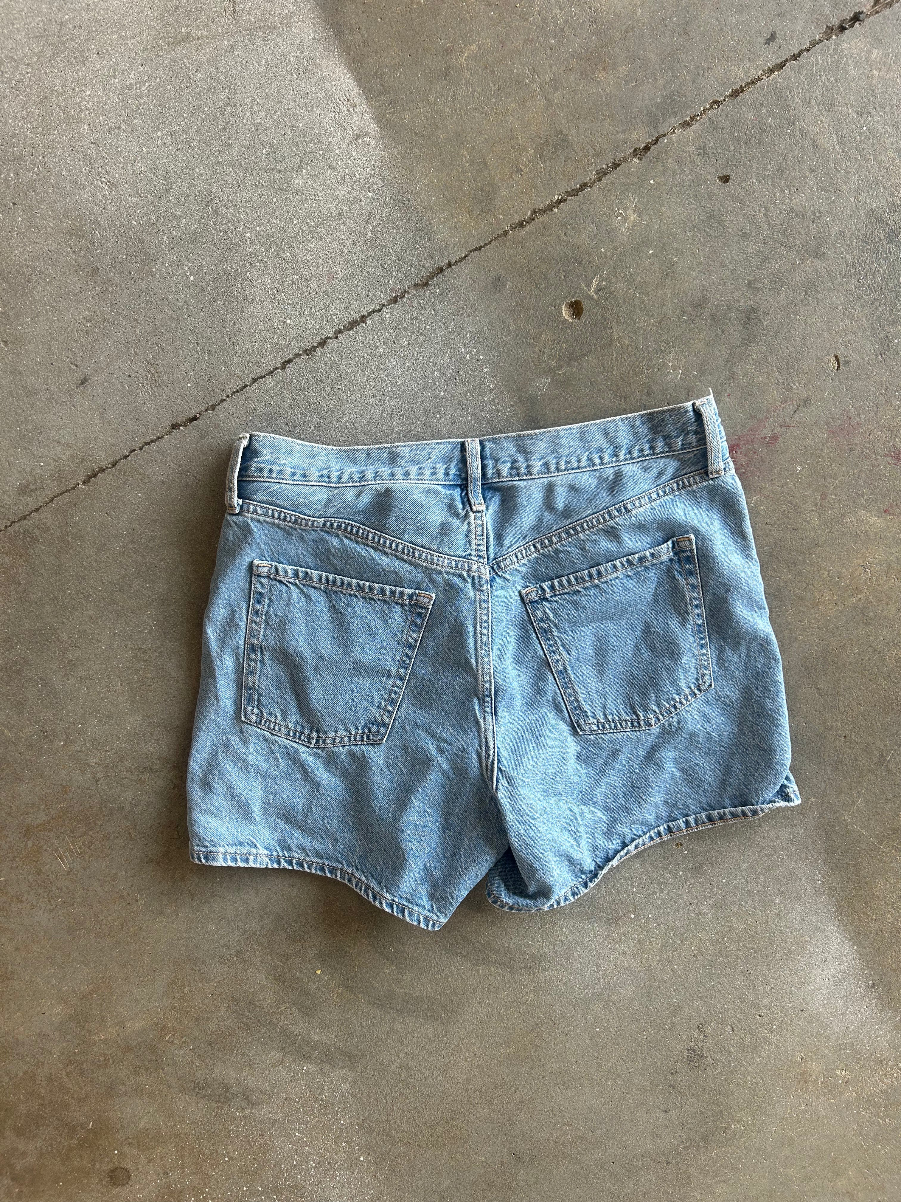 Light wash blue denim shorts shown from the back, laid flat on a concrete floor