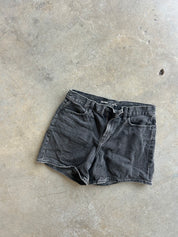 A pair of faded black denim shorts laid flat on a textured concrete floor