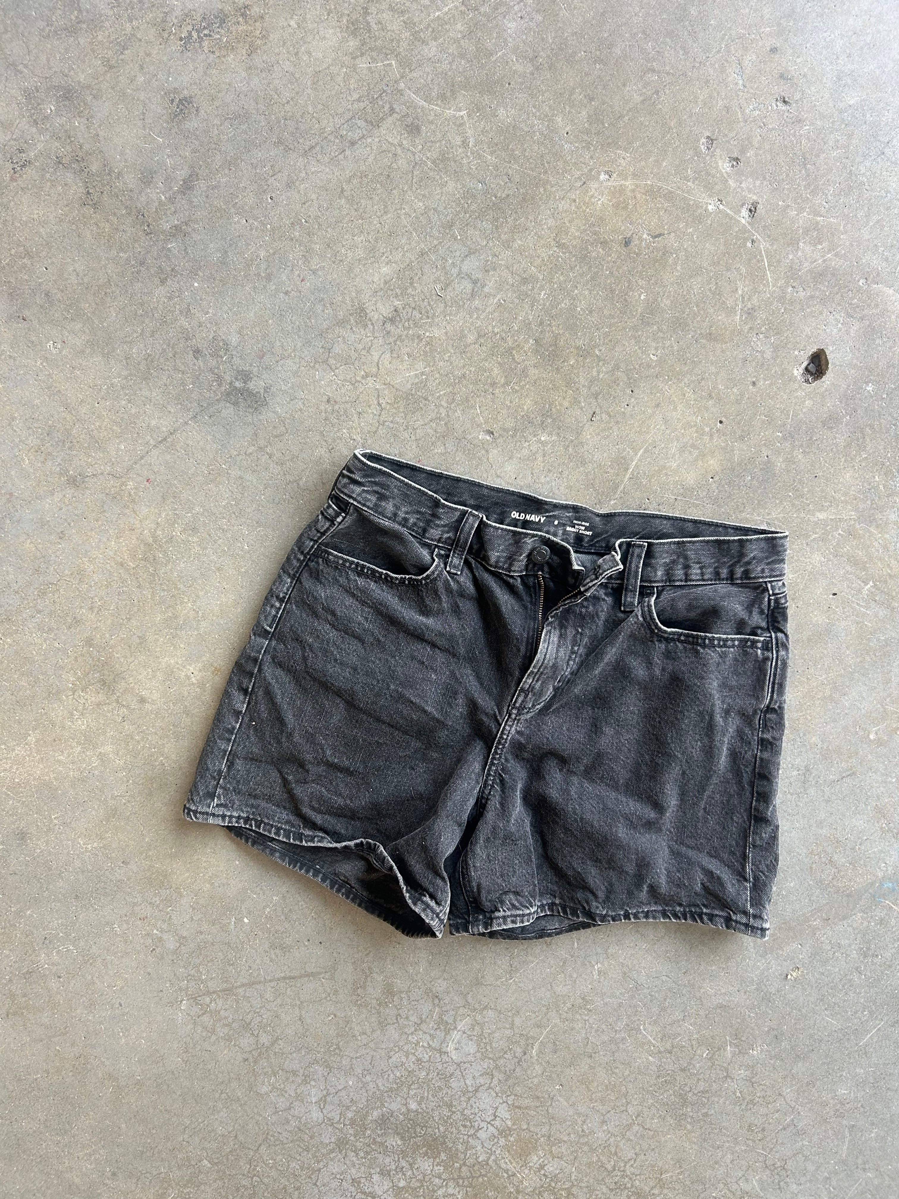 A pair of faded black denim shorts laid flat on a textured concrete floor