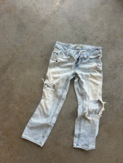 Light-wash distressed denim jeans laid flat on a concrete floor, featuring ripped details and frayed edges