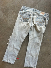 Light-wash distressed denim jeans shown from the back, laid flat on a gray concrete floor