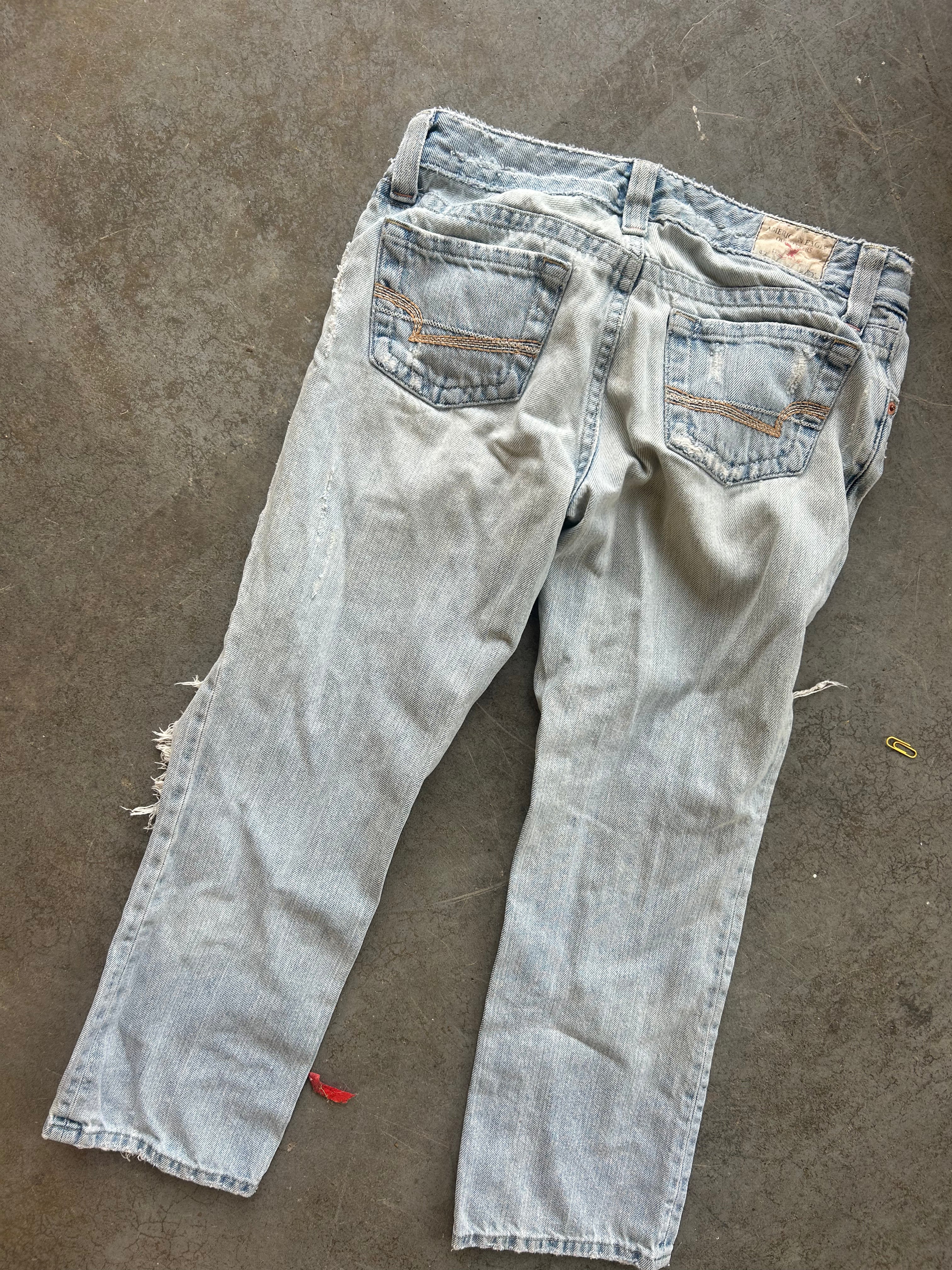 Light-wash distressed denim jeans shown from the back, laid flat on a gray concrete floor