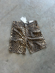 A pair of leopard print shorts with a white price tag attached, laid flat on a gray concrete floor