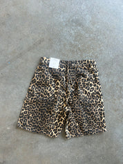 Leopard print shorts with a white brand tag, laid flat on a gray concrete floor