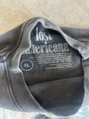 A close-up of a dark gray sweatshirt laid flat, showing the inside neck label with the text 'lost americana' and size 'XL'