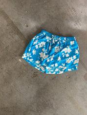 Blue floral swim trunks with a white daisy pattern, laid flat on a gray concrete floor