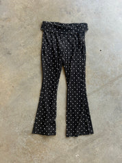 Black flared pants with a white polka dot pattern, laid flat on a textured concrete floor