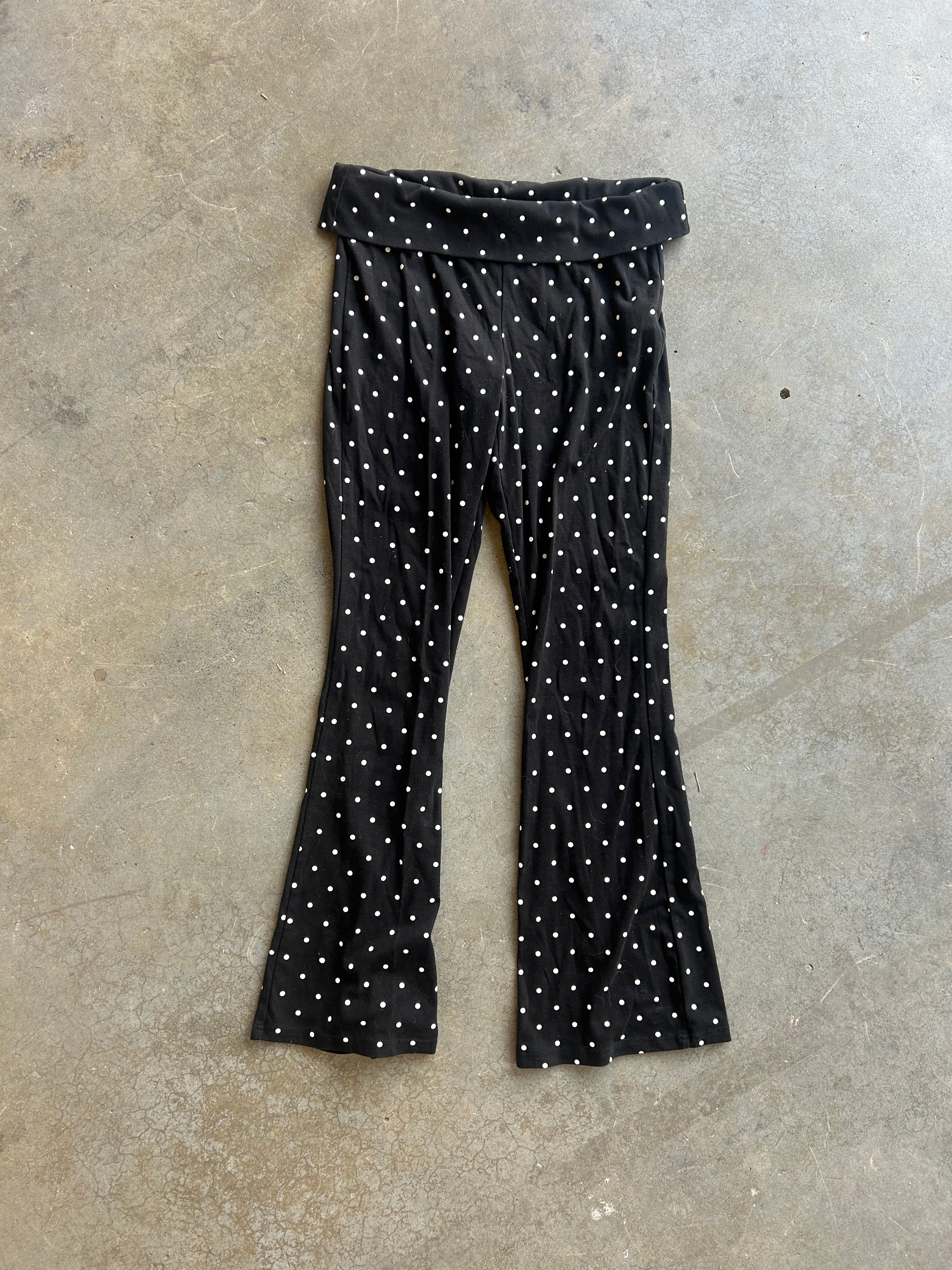 Black flared pants with a white polka dot pattern, laid flat on a textured concrete floor