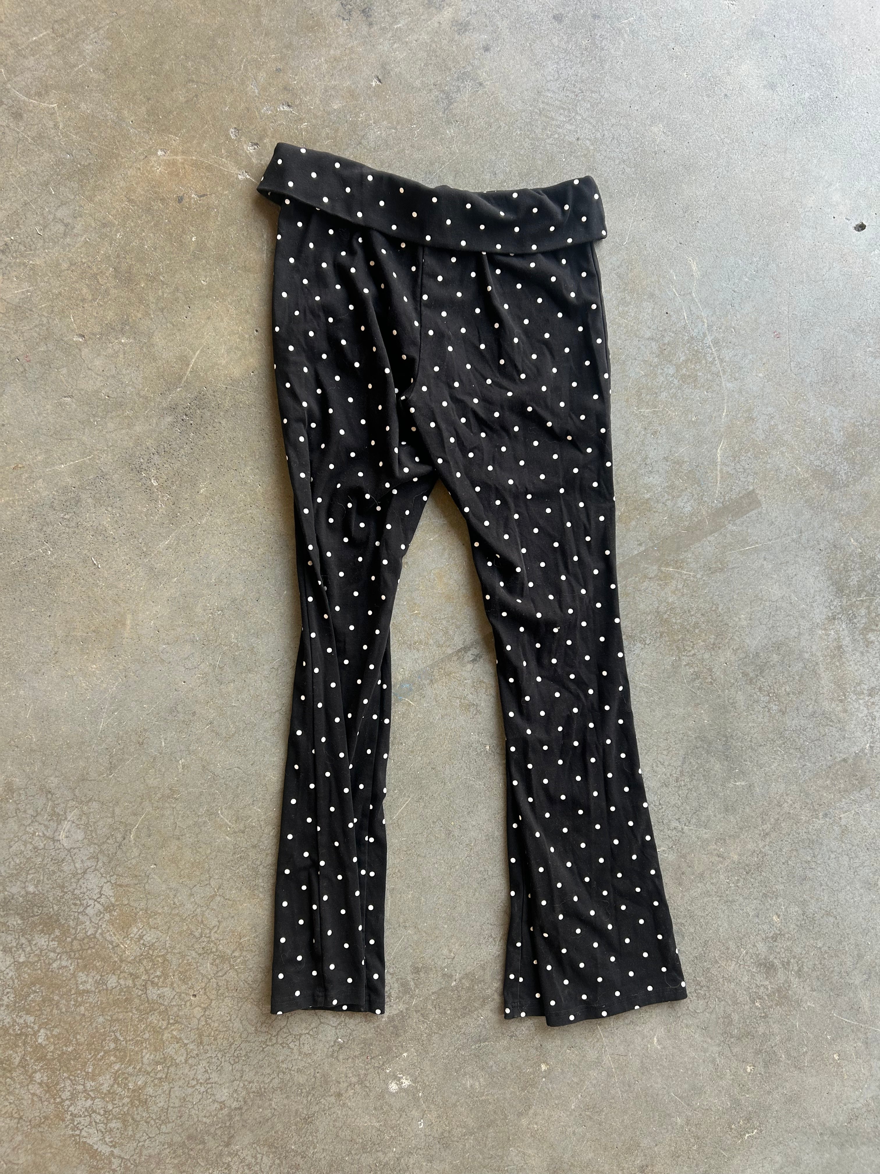 Black flared leggings with a white polka dot pattern, laid flat on a textured concrete floor
