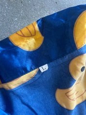 A close-up of a blue fabric garment, likely a shirt or shorts, featuring a yellow duck print and a small white size tag marked 'L'