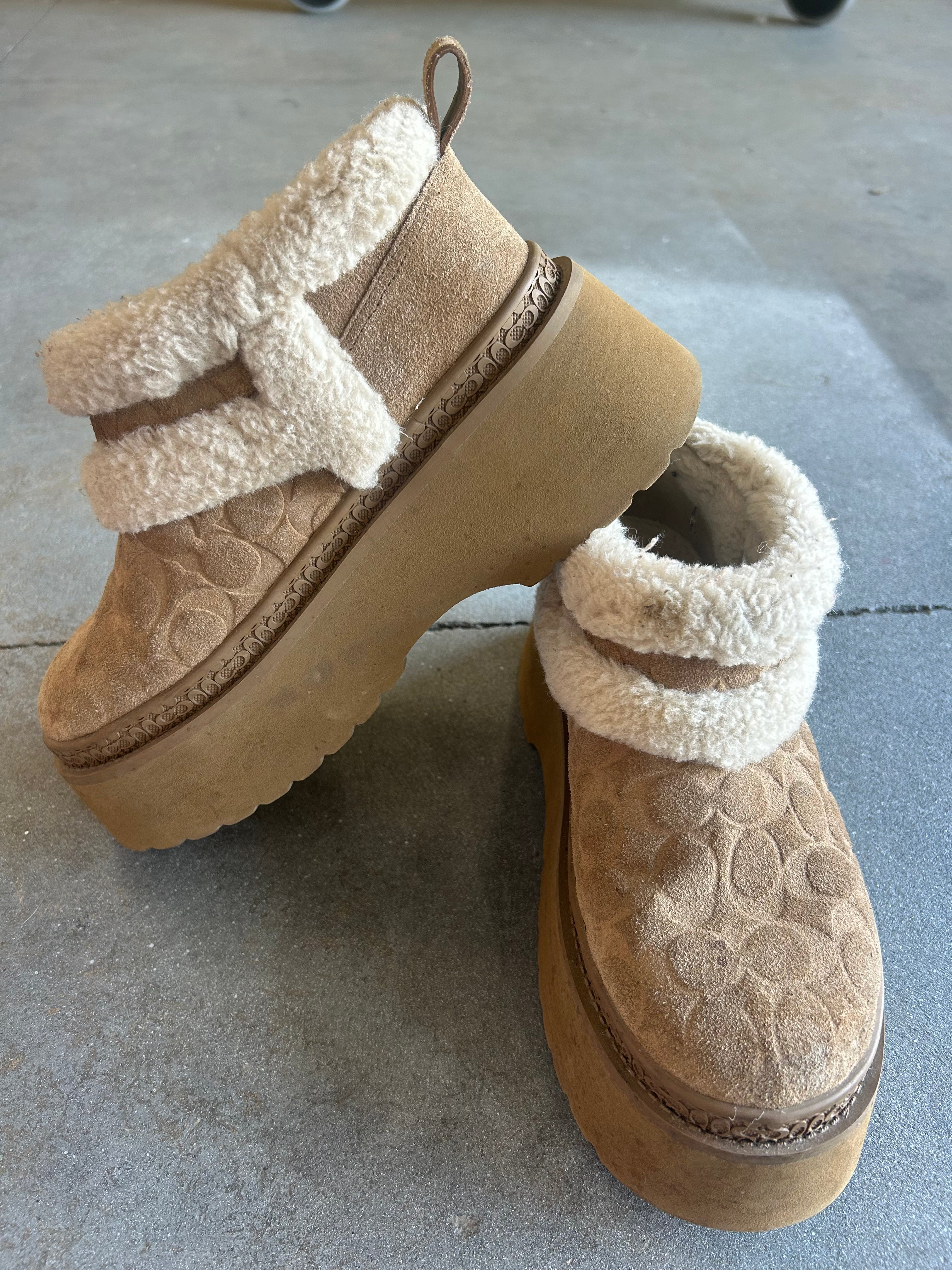 A pair of beige platform ankle boots with a cream sherpa fleece lining and a textured embossed pattern on the sides, displayed on a gray concrete floor