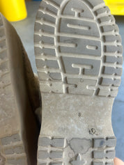 Close-up of the dirty gray rubber outsole of a boot, showing tread patterns and a small circular defect near the lower center