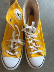 A pair of yellow Converse high-top sneakers with white laces and white rubber toe caps, photographed from above on a gray concrete floor