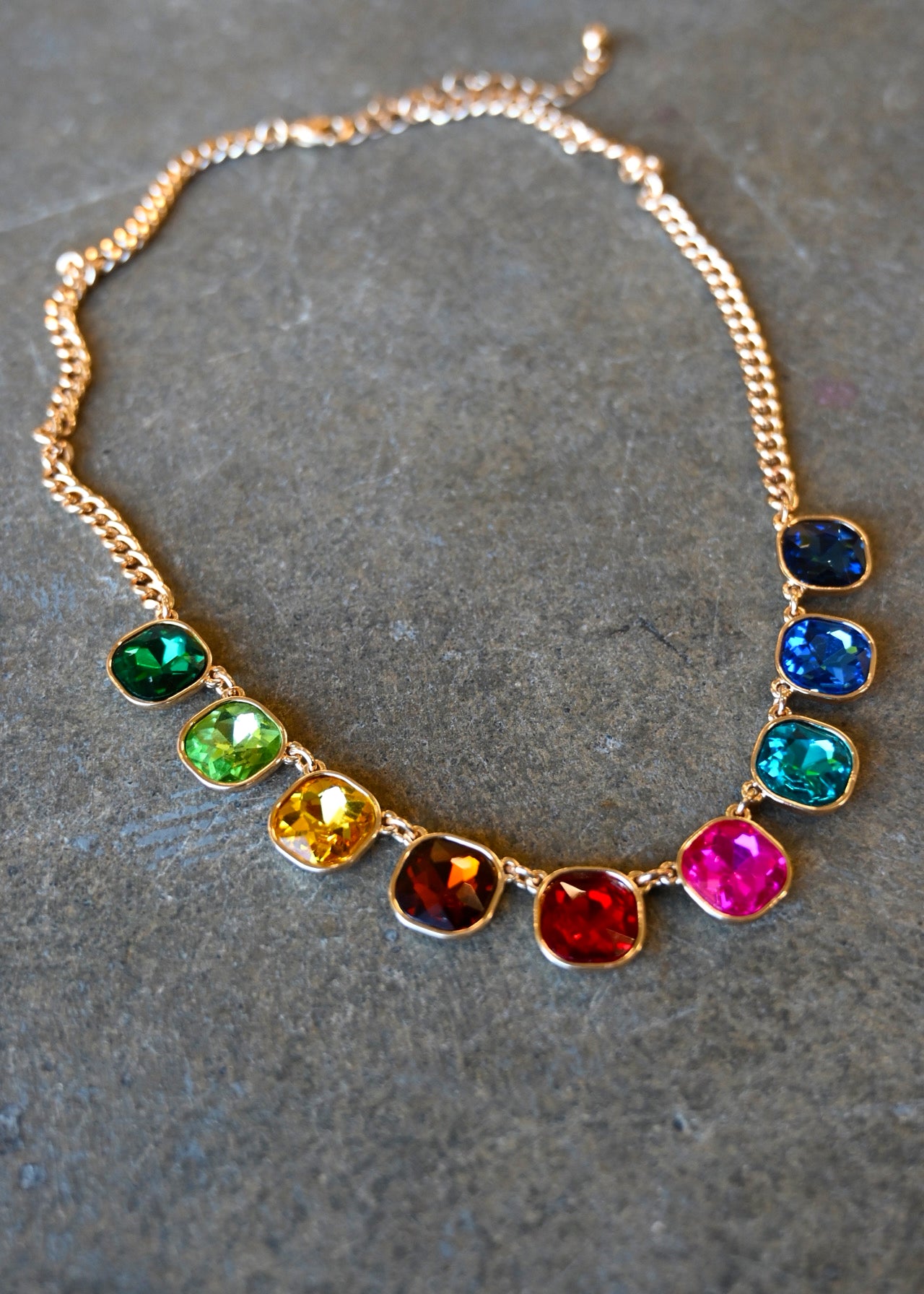 Close up of a gold necklace with multi-color cushion cut gemstones on a dark background