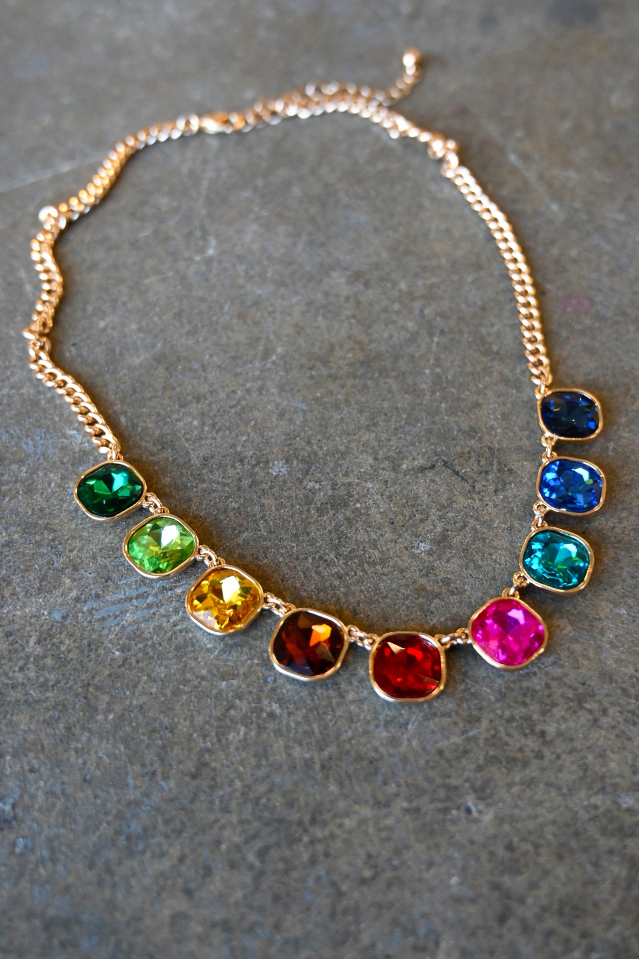 Close up of a gold necklace with multi-color cushion cut gemstones on a dark background