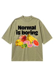 A light khaki t-shirt with a graphic print that reads 'Normal is boring' in bold black text above a colorful assortment of fruits including bananas, kiwi, grapefruit, and melon, flat lay frontal view