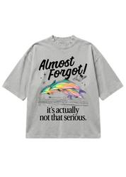 Gray oversized short sleeve shirt with a colorful dolphin graphic and 'Almost Forgot! it's not that serious." text on a white background, flat lay frontal view