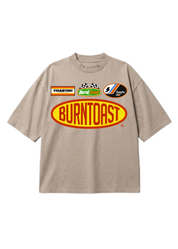 A beige short-sleeve t-shirt with a large 'BUNTOAST' graphic on the front, featuring smaller sponsor-style logos above it, displayed against a solid white background