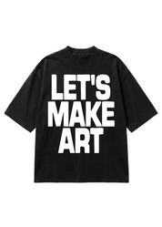 A black short-sleeve t-shirt with the phrase 'LET'S MAKE ART' printed in large, bold white block letters across the front, displayed on a solid white background
