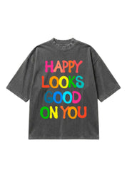 Gray graphic short sleeve shirt with colorful text 'Happy Looks Good On You' on a white background, flat lay frontal view