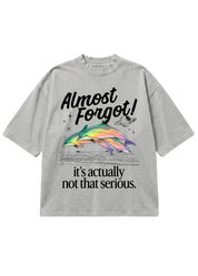 Gray oversized short sleeve shirt with a colorful dolphin graphic and 'Almost Forgot! it's not that serious." text on a white background, flat lay frontal view