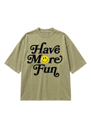 An oversized short-sleeve t-shirt in a washed olive green color, featuring the phrase 'Have More Fun' printed in black script across the chest, with a small yellow smiley face graphic replacing the letter 'o'