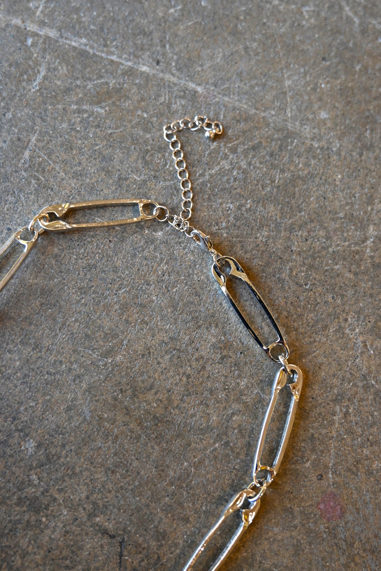 Close up of a silver necklace made of safety pins with a clasp on a dark background