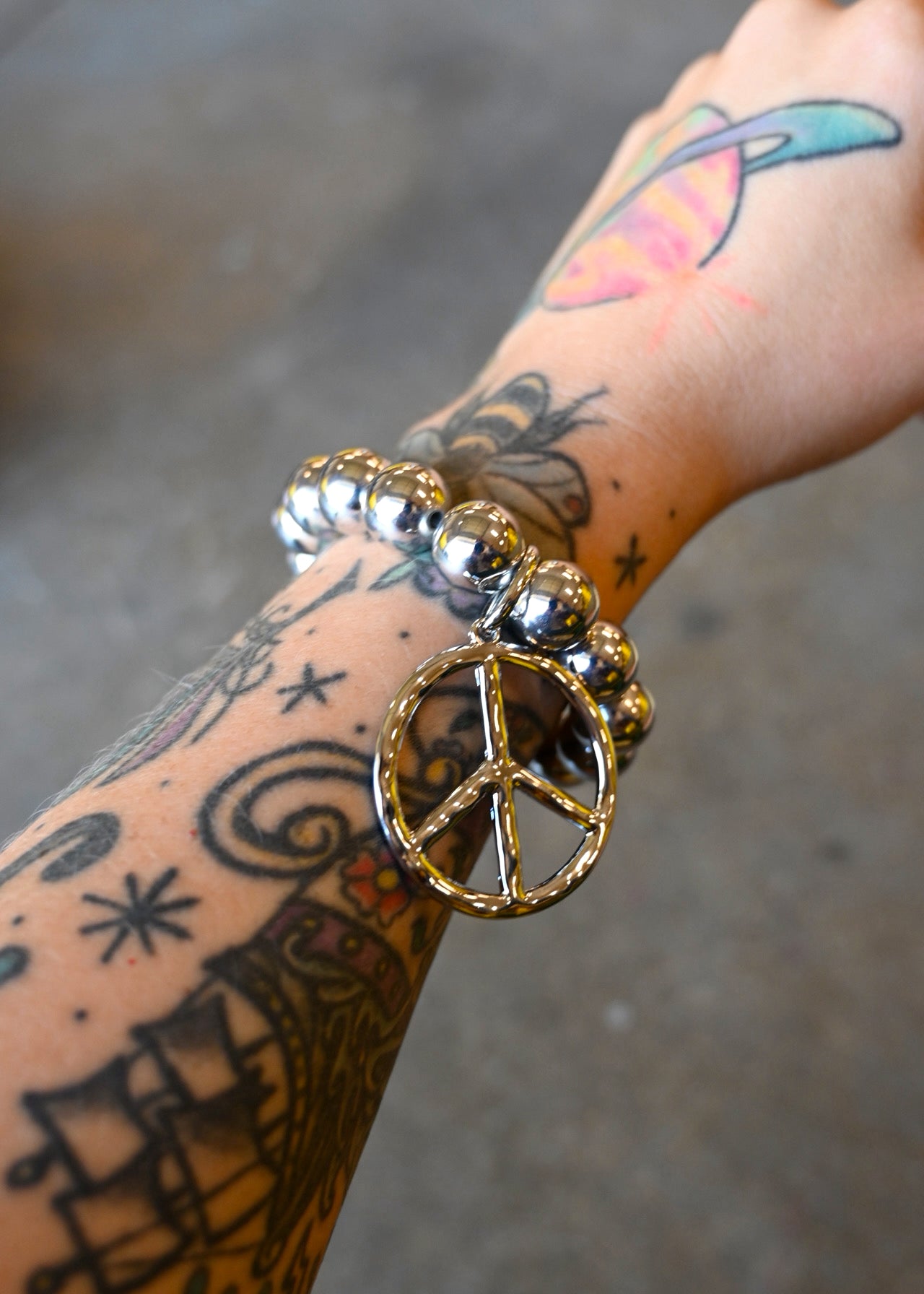 A model wearing a  silver beaded bracelet with a peace sign charm on a dark background