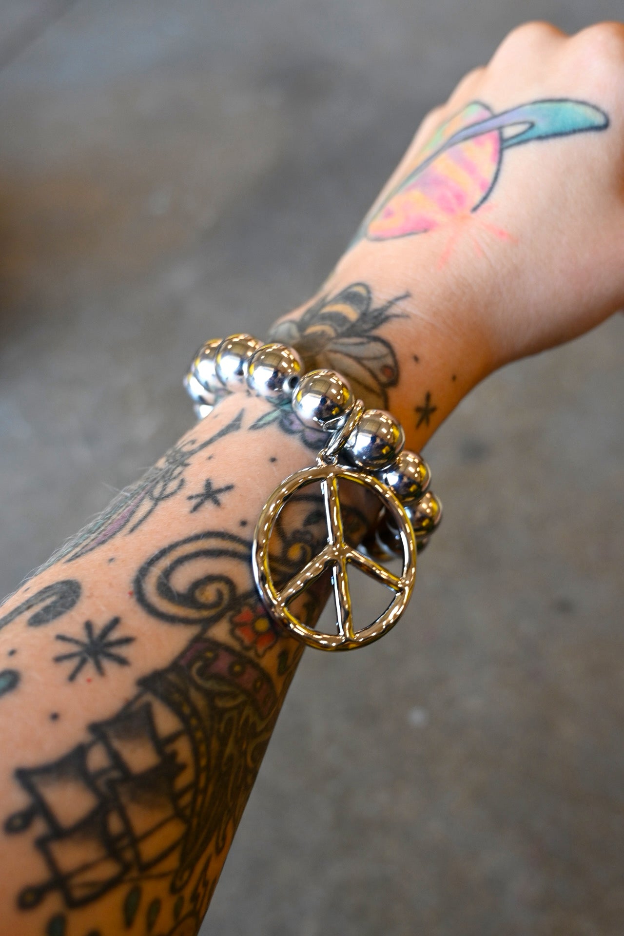 A model wearing a  silver beaded bracelet with a peace sign charm on a dark background