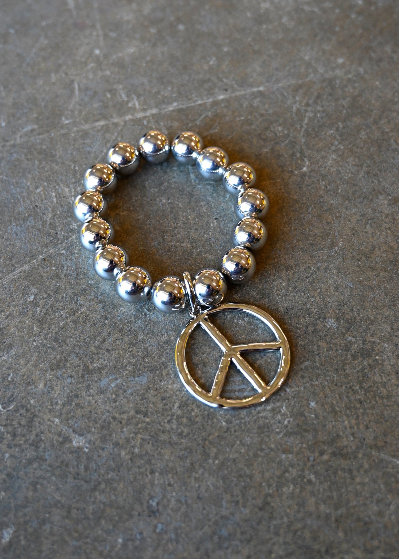 A silver beaded bracelet with a peace sign charm on a dark background