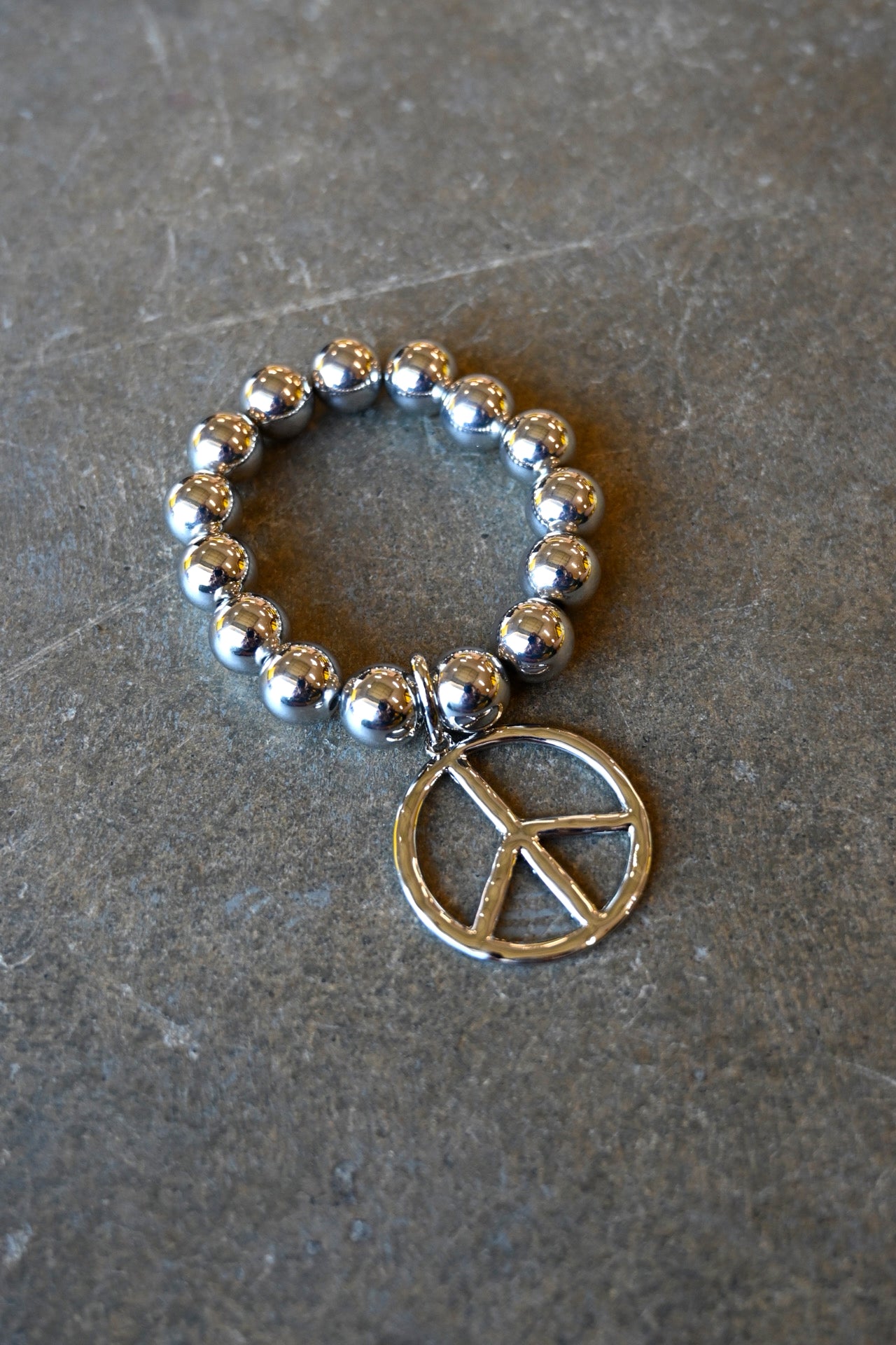 A silver beaded bracelet with a peace sign charm on a dark background
