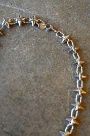 Close up of a silver necklace with spike studs around it on a dark background