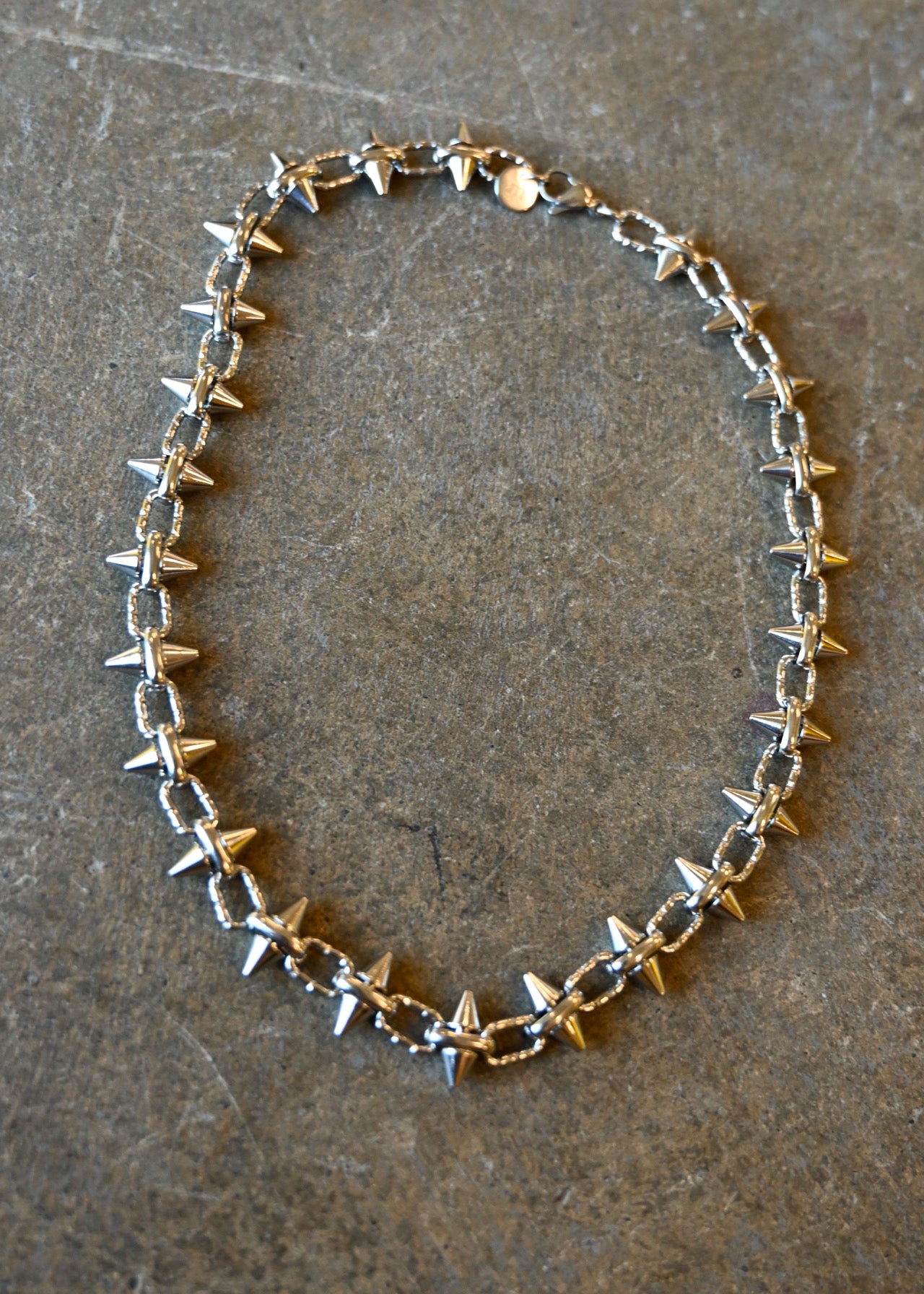 A silver necklace with spike studs around it on a dark background