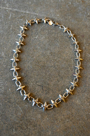 A silver necklace with spike studs around it on a dark background