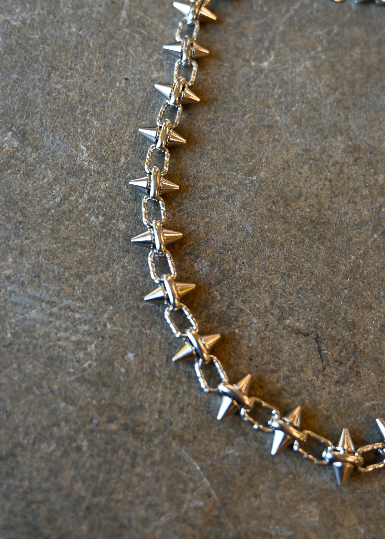 Close up of a silver necklace with spike studs around it on a dark background