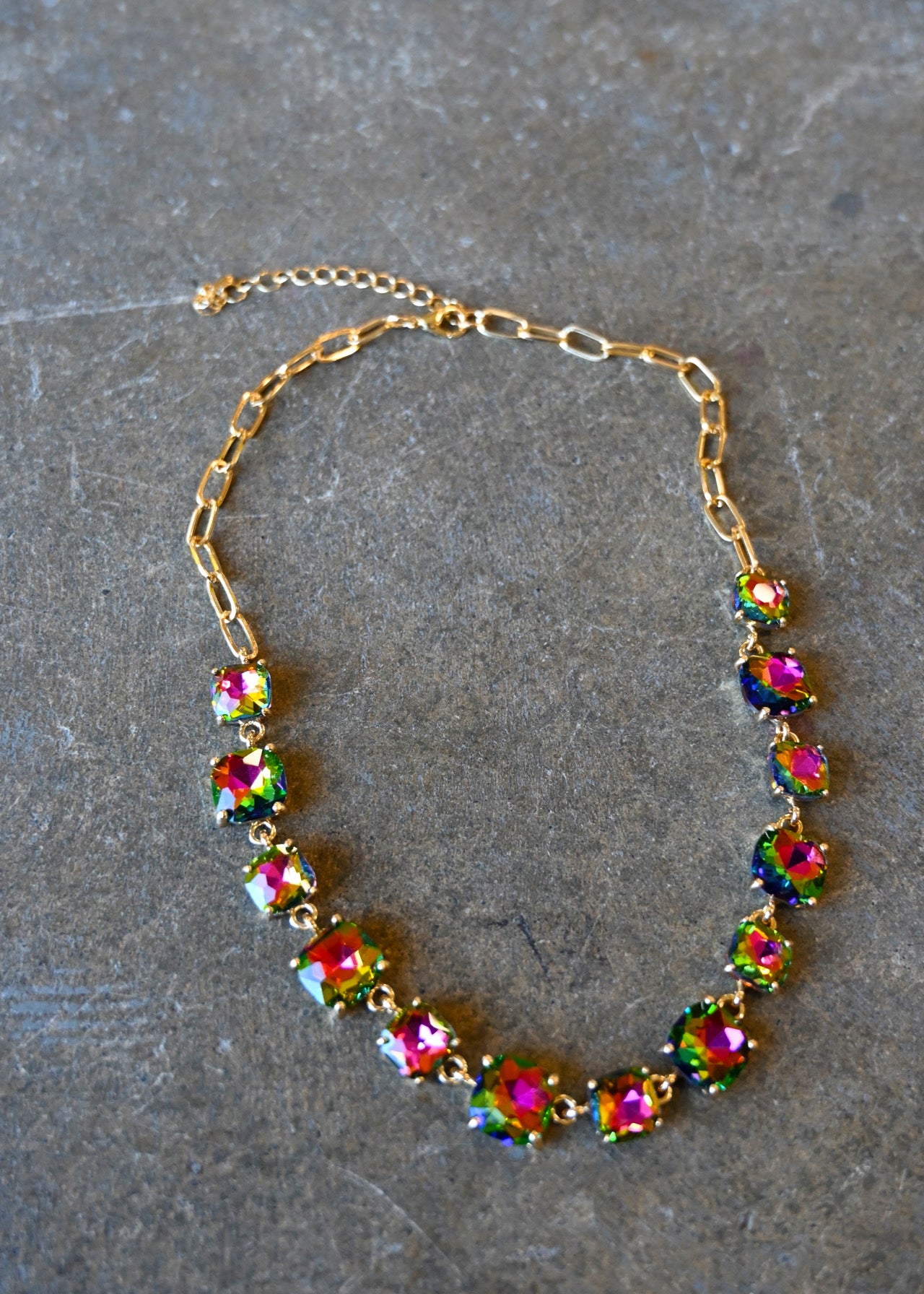 A gold bracelet made of multi-color square gems on a dark background