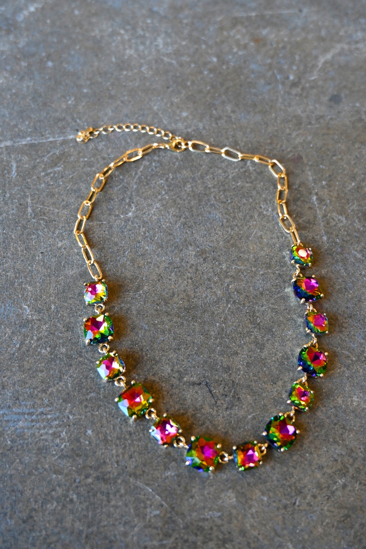 A gold bracelet made of multi-color square gems on a dark background