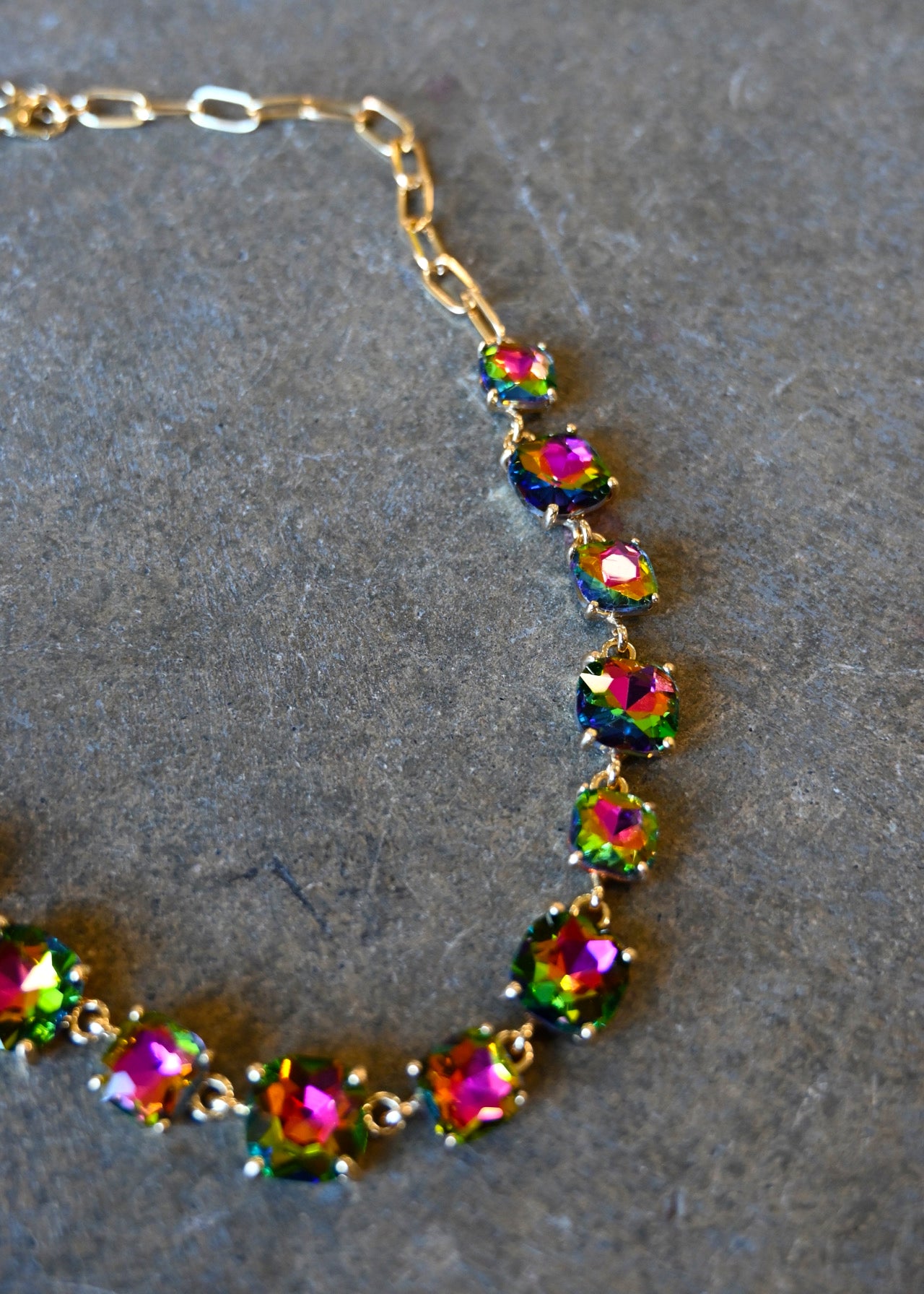 Close up of a gold bracelet made of multi-color square gems on a dark background