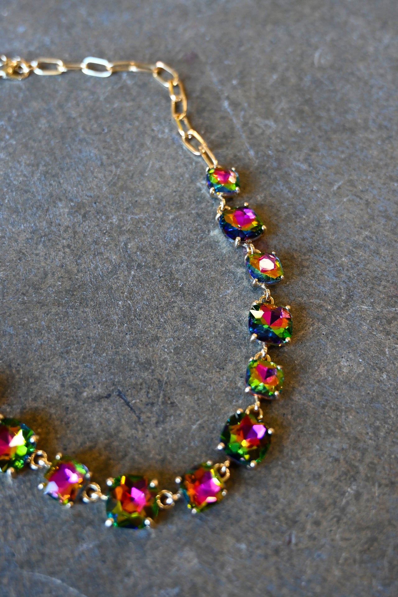 Close up of a gold bracelet made of multi-color square gems on a dark background