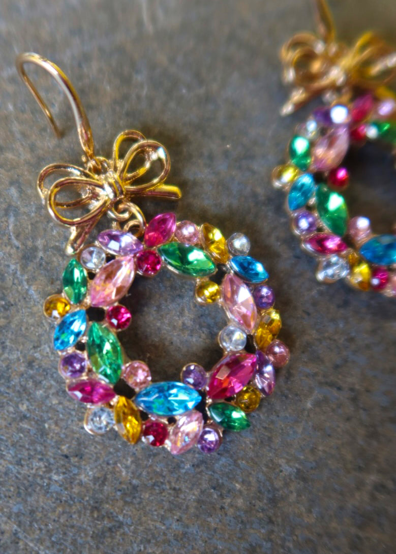 Close up of a pair of gold earrings with multicolored wreaths on a dark surface