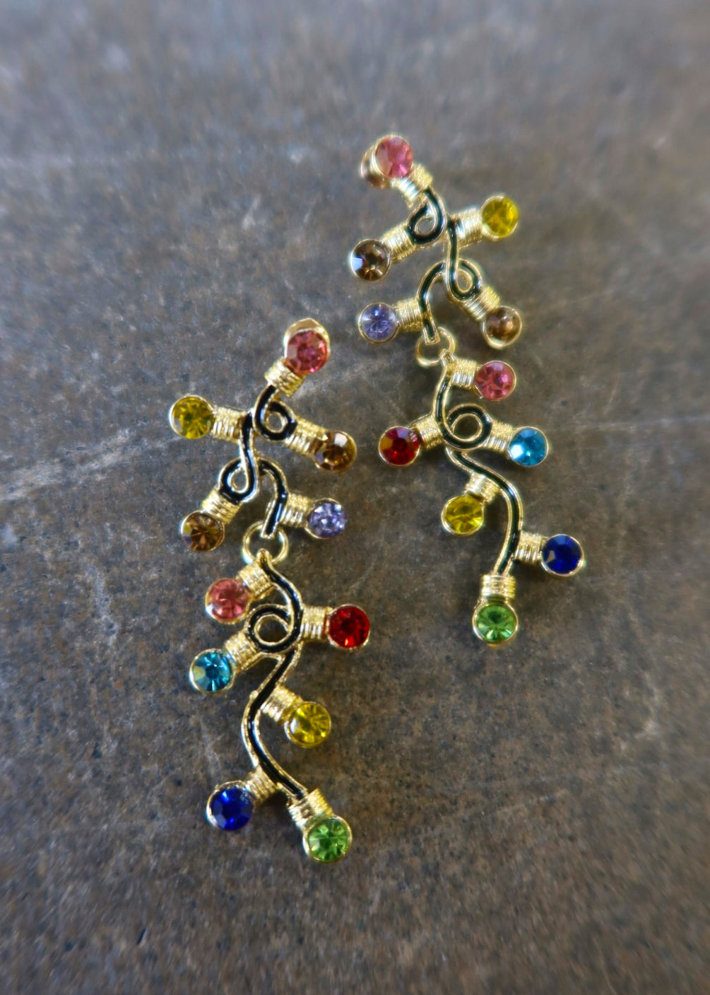 Pair of gold dangly earrings with a string of lights with multi-colored studs on a dark background