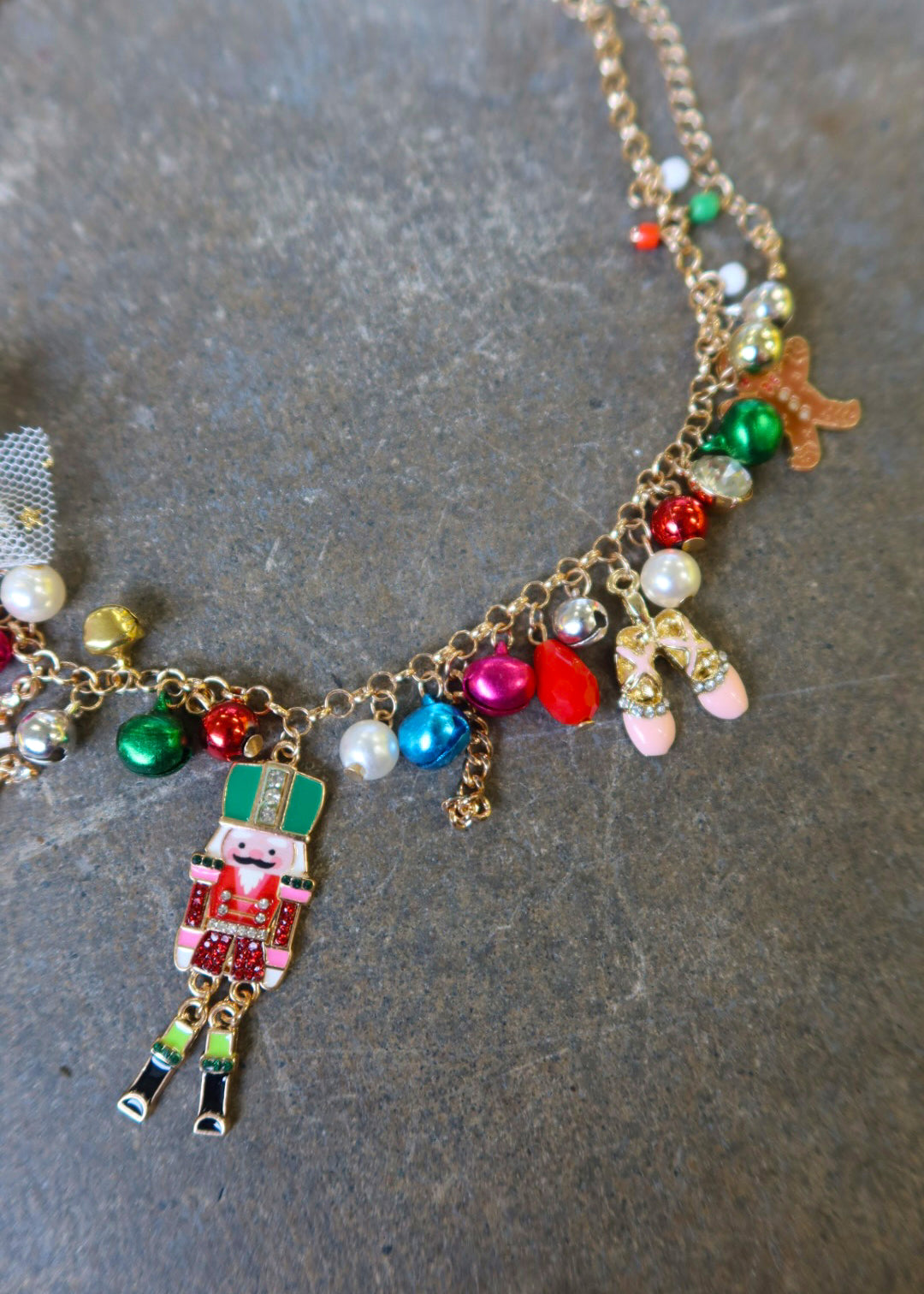 Close up of a gold necklace with multicolor jewels and a nutcracker and white bow on a dark surface
