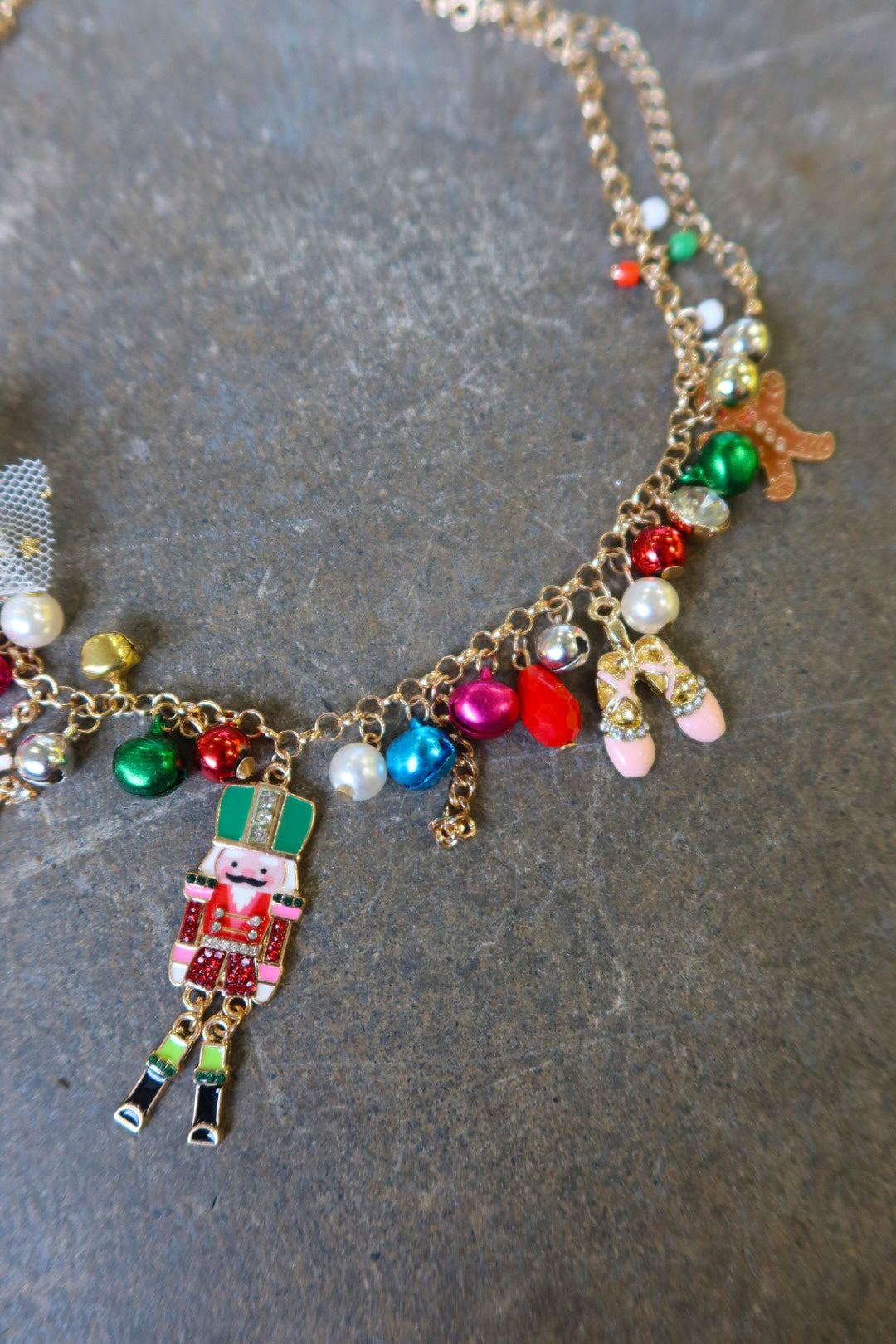 Close up of a gold necklace with multicolor jewels and a nutcracker and white bow on a dark surface