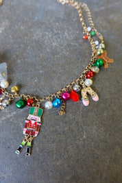 Close up of a gold necklace with multicolor jewels and a nutcracker and white bow on a dark surface