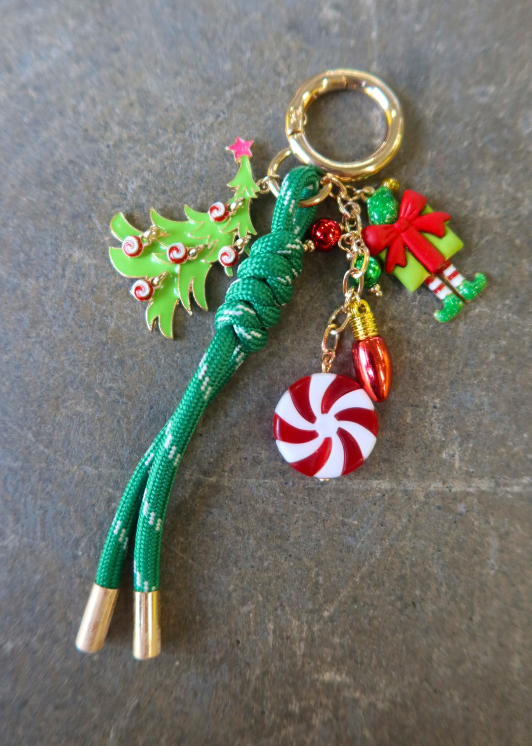 A gold ring bag charm with different Christmas charms on a dark surface